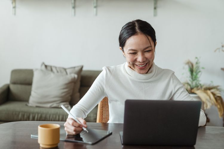 Person smiling and working on a laptop and table at home.