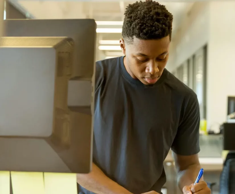 man on writing on notepad next to monitor