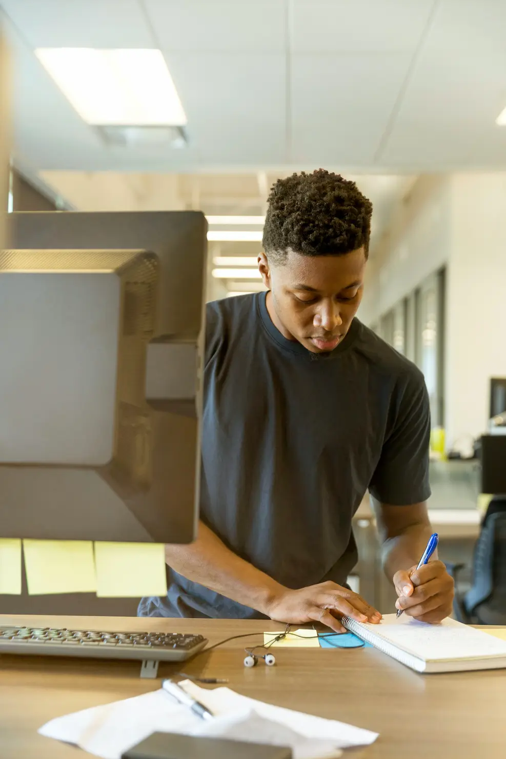 man on writing on notepad next to monitor