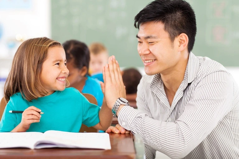 A male teacher high-fiving a student in a classroom.