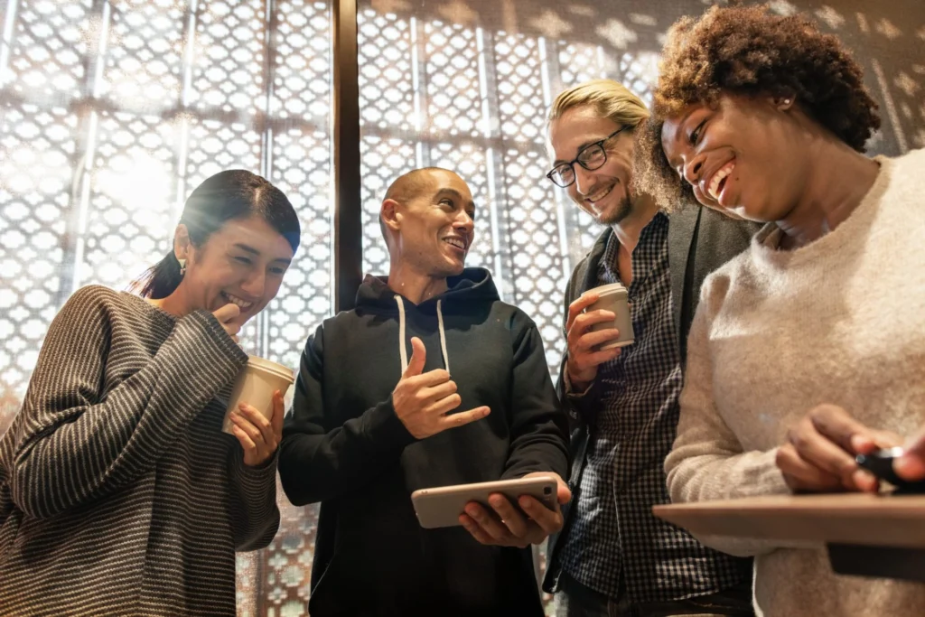 A diverse group of four employees smiling and interacting in a casual office setting.