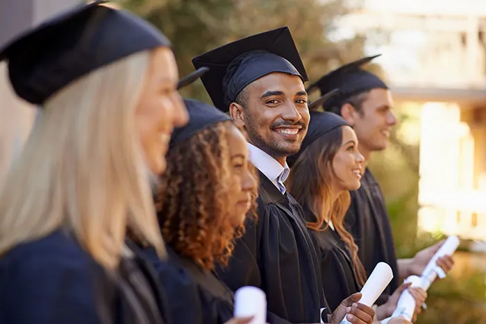Graduates in caps and gowns holding diplomas, smiling and standing in a line