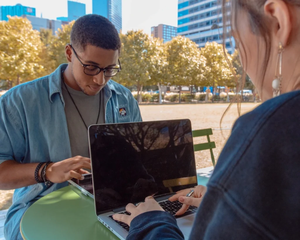 A young man and woman working on laptops at a table outdoors, symbolizing Gen Z's flexible and tech-savvy lifestyle.