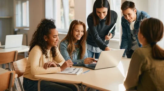 Students gathered at table using laptop