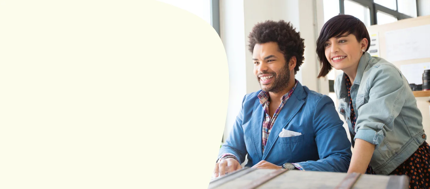 Two colleagues smiling while working at desktop computer