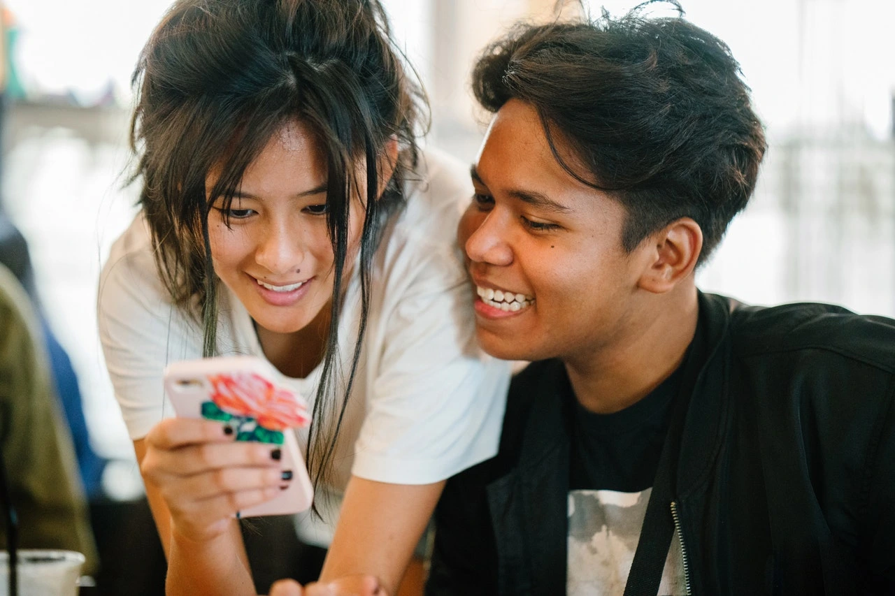 Two Gen Z individuals smiling and looking at a smartphone together.