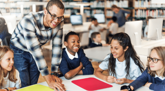 Male teacher working with young students at table